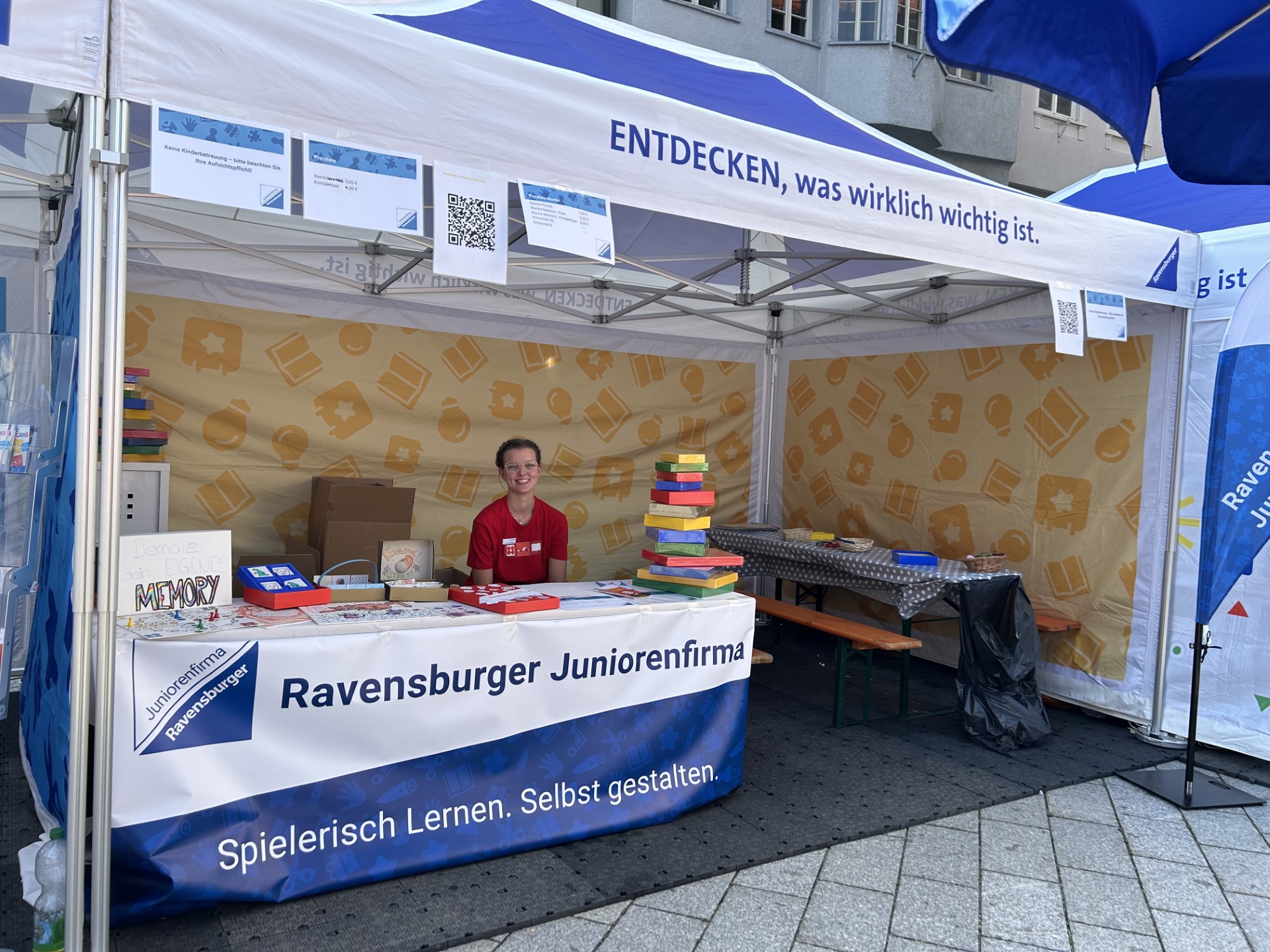 Eine Person sitzt hinter dem Stand der Ravensburger Juniorenfirma bei Ravensburg Spielt